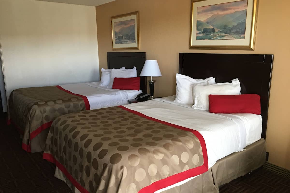 A hotel room with two beds, a nightstand, a lamp, and two framed pictures on the wall.