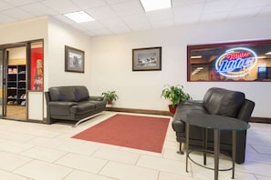 A lobby with a red carpet, two leather sofas, a glass coffee table, framed pictures, and a Miller Lite sign. - Budget Inn Laramie (Laramie)