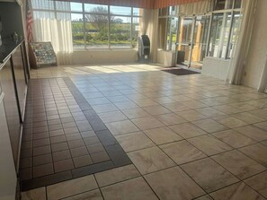 A spacious lobby with a tiled floor, a reception desk, and large windows offering a view of the outdoors. - Heritage Inn & Suites by Capital O Baton Rouge I 10 (Baton Rouge)