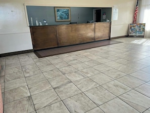 A reception area with a wooden reception desk, a framed picture on the wall, and a tiled floor. - Heritage Inn & Suites by Capital O Baton Rouge I 10 (Baton Rouge)