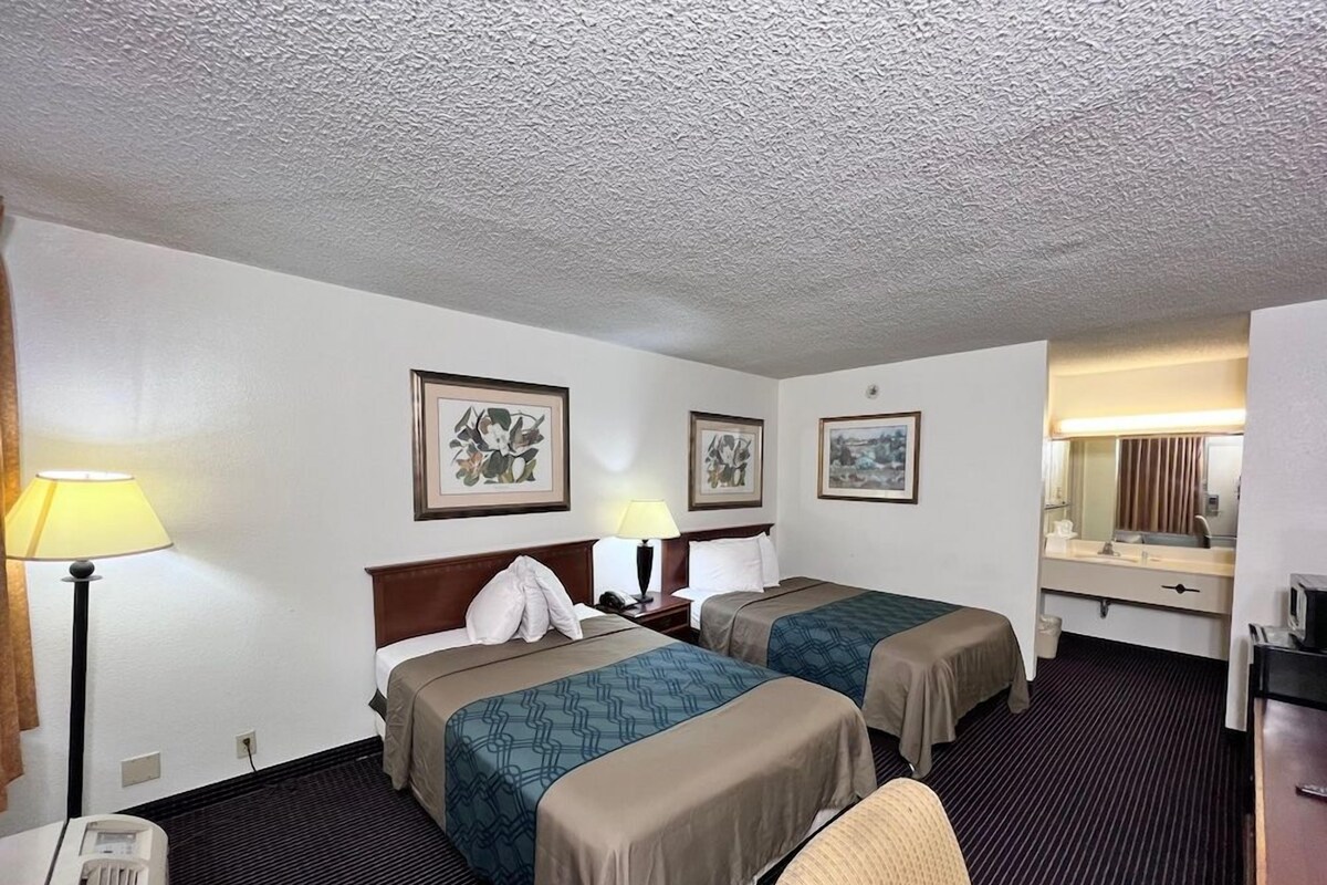 A hotel room with two beds, a desk, a chair, a lamp, and a mirror.
