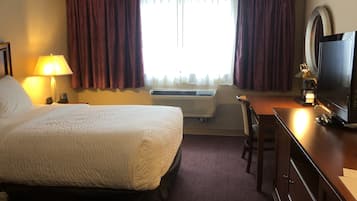 Ett hotellrum med en säng, ett skrivbord, en tv, en lampa och en luftkonditioneringsanläggning.