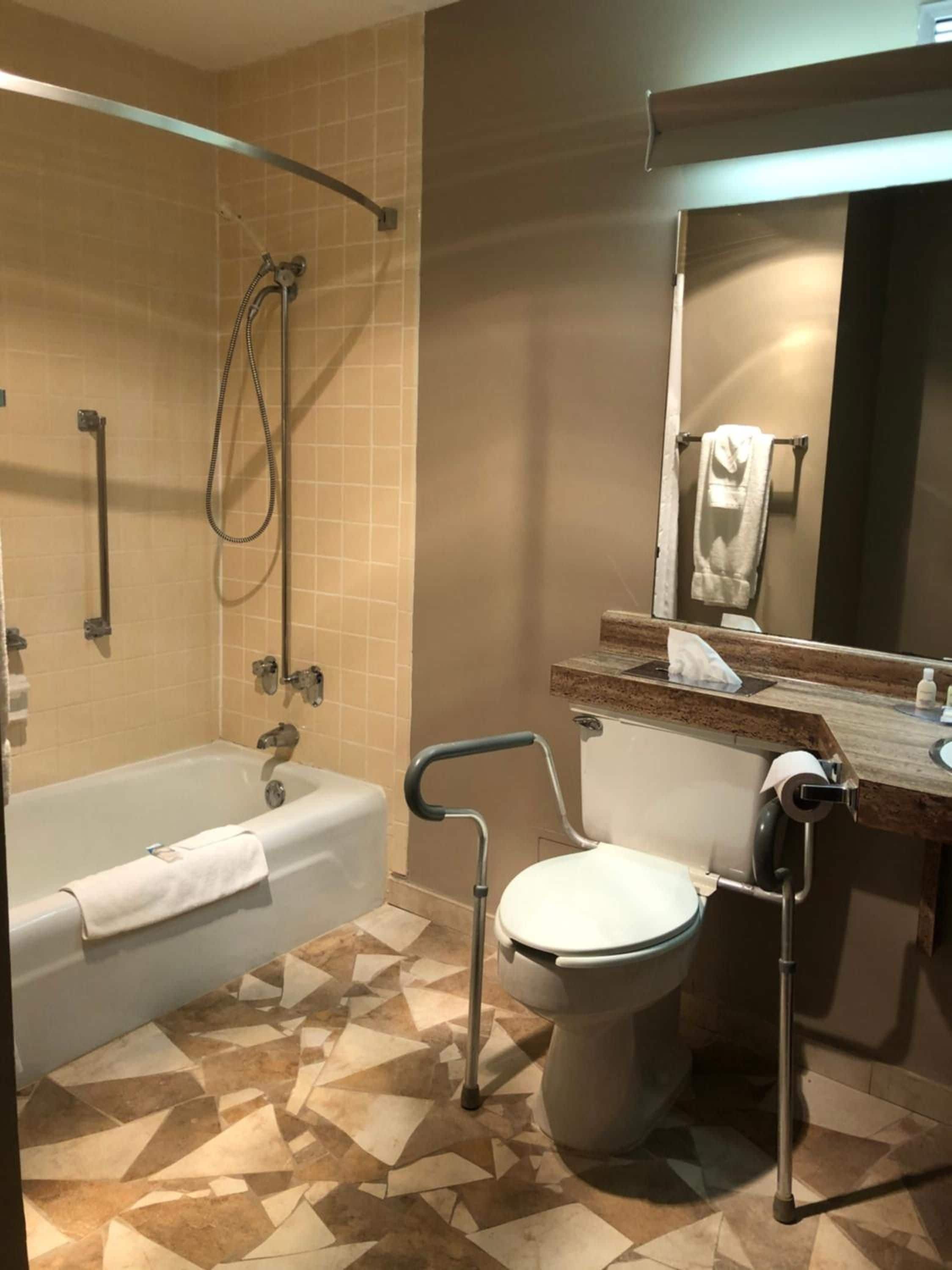 A bathroom with a bathtub, a toilet with a grab bar, a shower area, and a mirror.