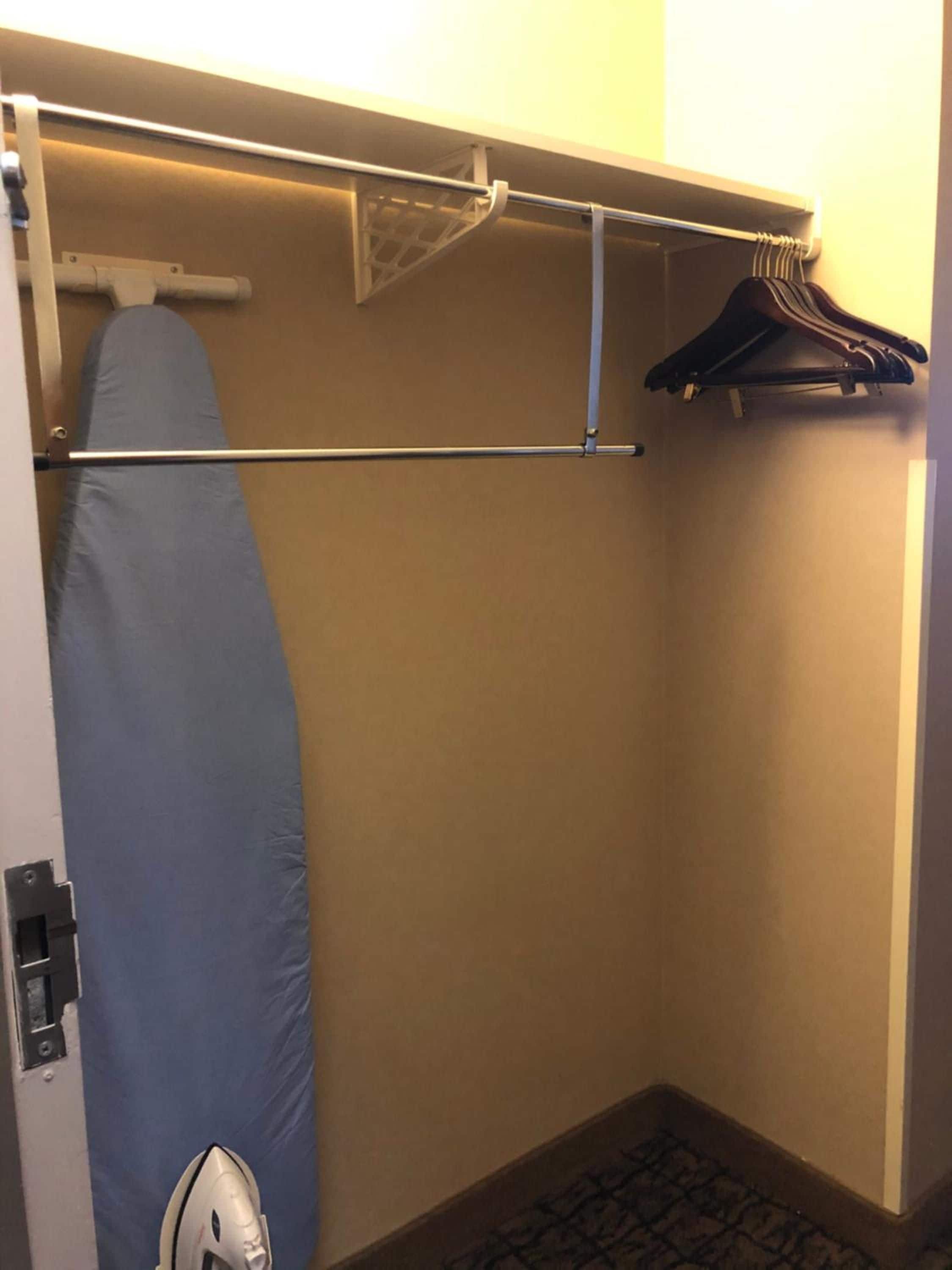 Habitación de hotel con ducha, tabla de planchar y perchero con ropa.