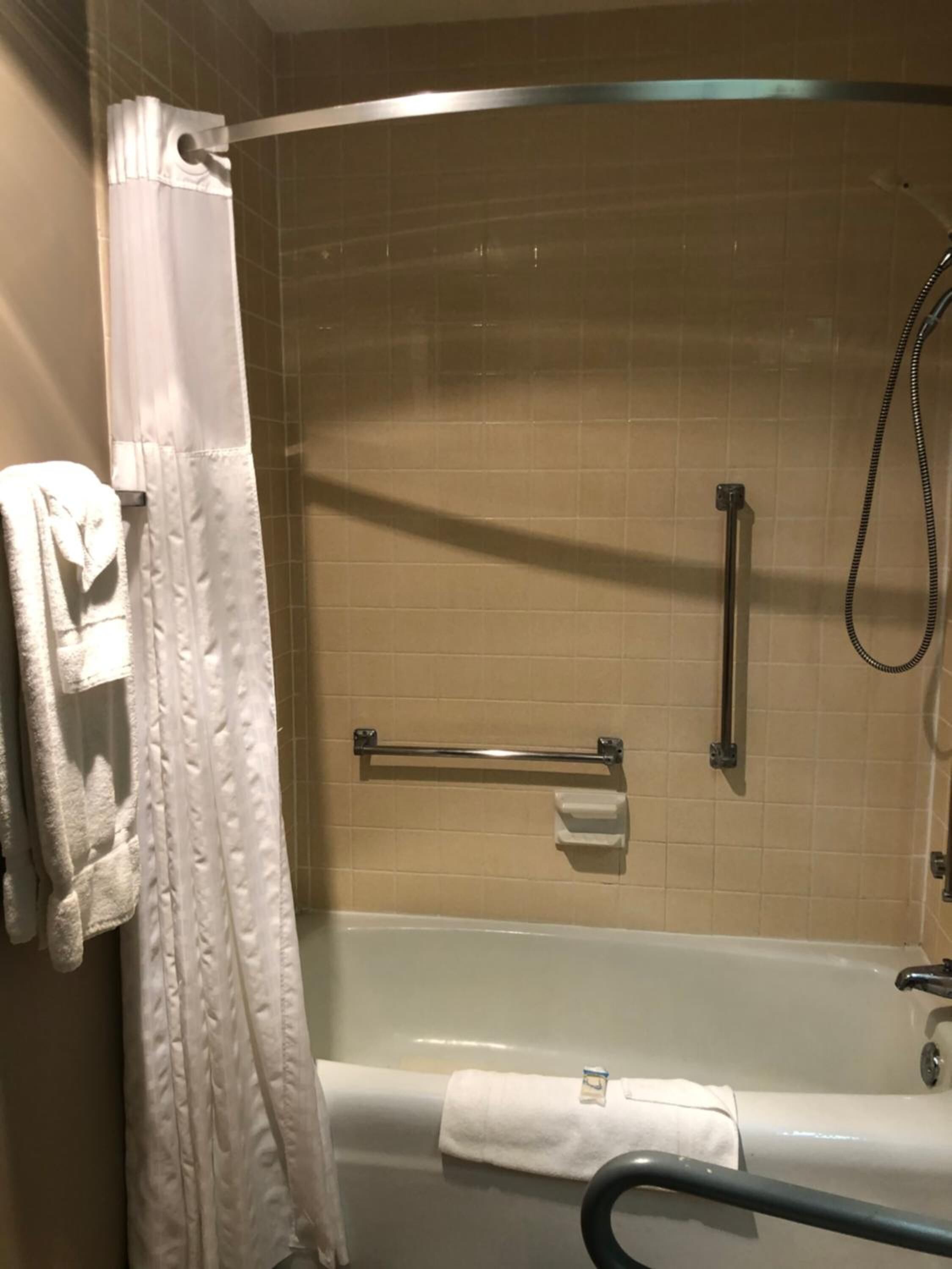 A bathroom with a bathtub, a shower, and a handrail.