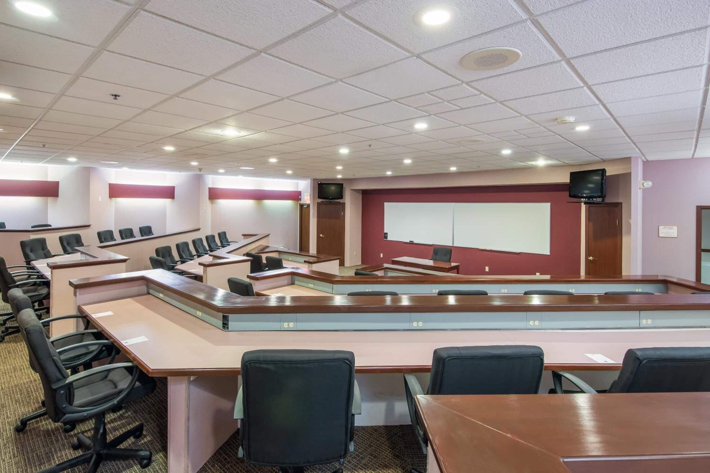 A conference room with multiple tables and chairs, a whiteboard, and a television on the wall.