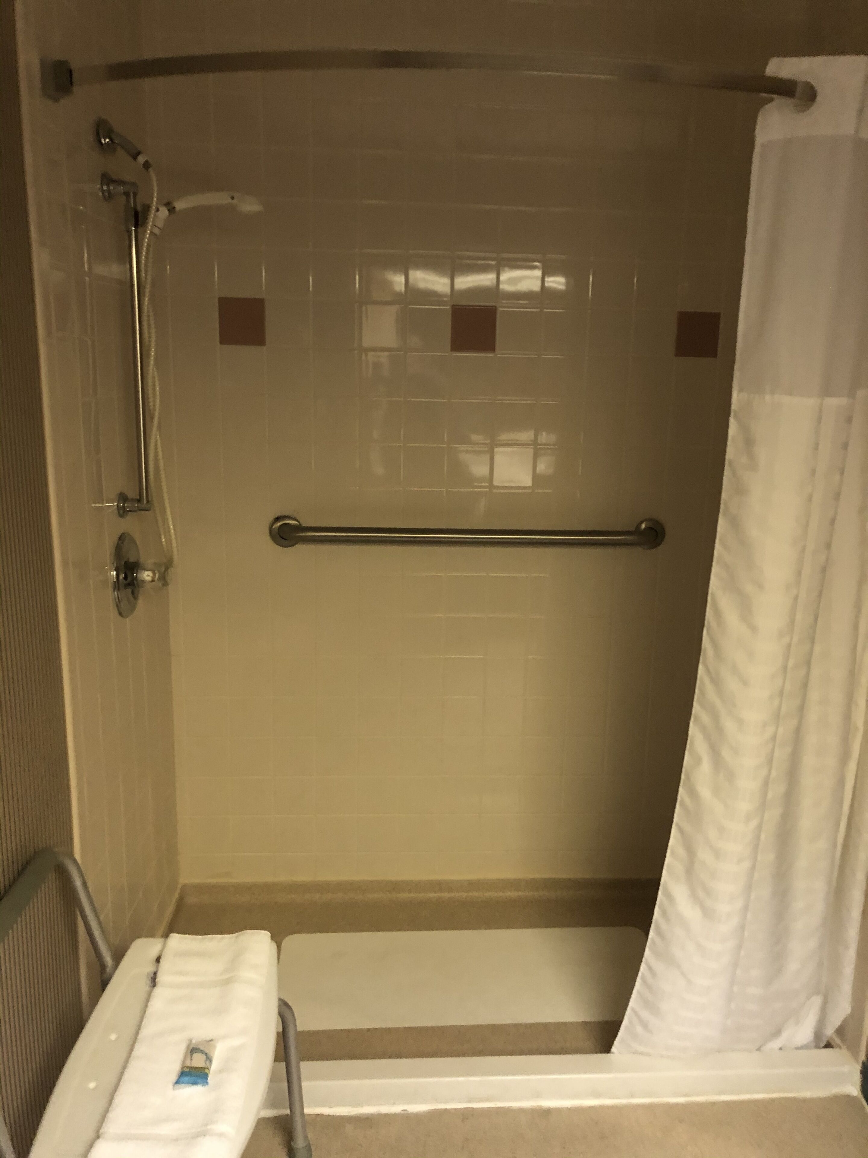 A shower area with a grab bar, a towel rack, and a shower curtain.