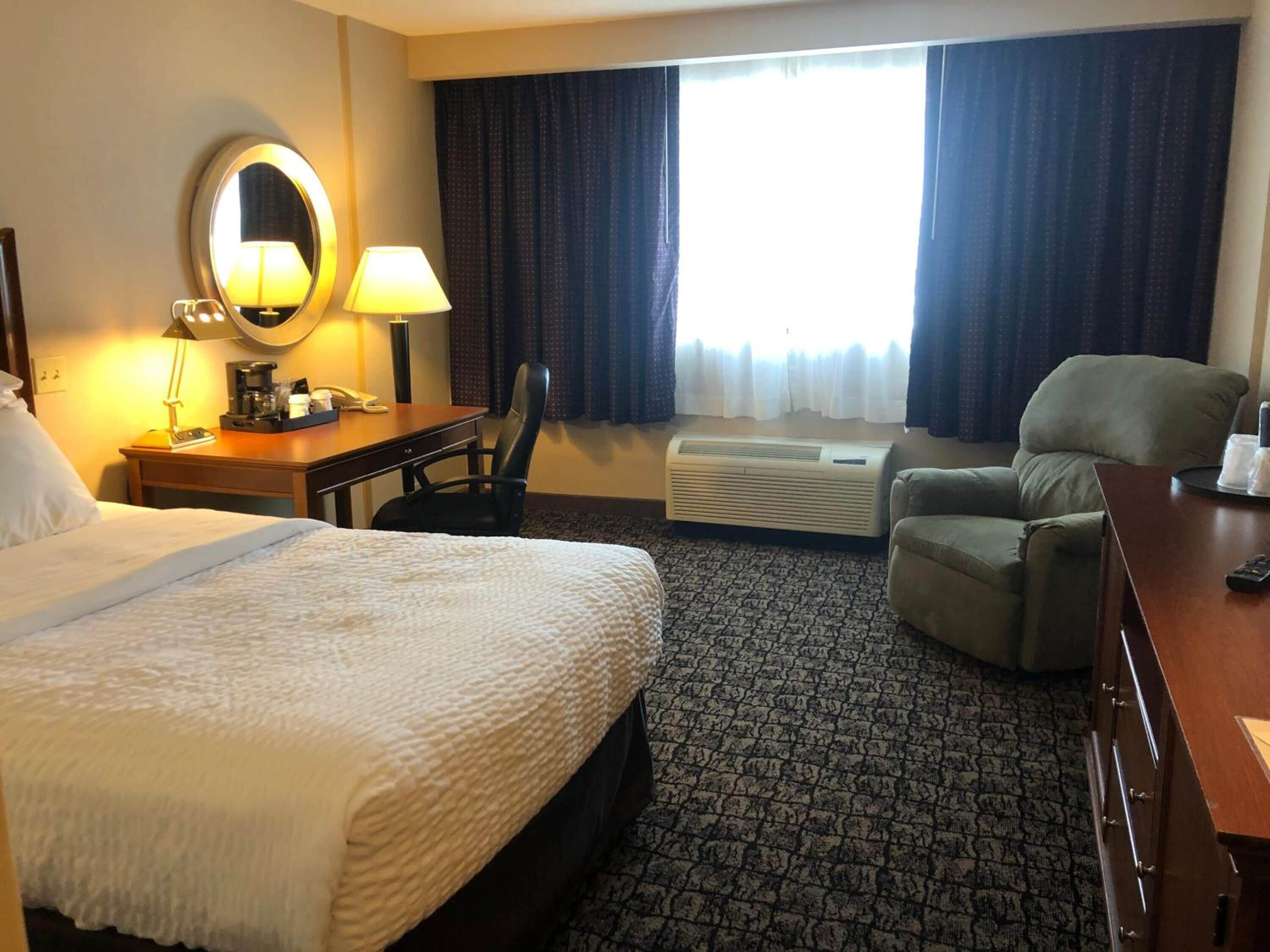 Een hotelkamer met een bed, bureau, stoel en een airconditioning.