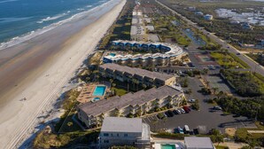 An aerial view of a coastal hotel with a beachside location, multiple swimming pools, and a parking area. - Coquina A203- Steps to the Beach (Saint Augustine)