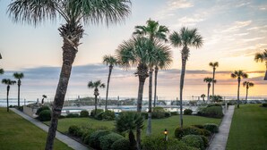 A landscaped area with palm trees, a pathway, and a view of the ocean at sunset. - Coquina A203- Steps to the Beach (Saint Augustine)