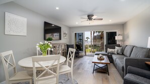 A modern living room with a grey sofa, white chairs, a round table, and a ceiling fan. - Coquina A203- Steps to the Beach (Saint Augustine)