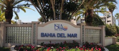Letrero que dice "ISIA DEL SOL BAHIA DEL MAR" con un arco decorativo y un parterre de flores al frente.
