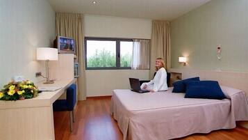 Una habitación de hotel con una cama, un escritorio, una silla, una computadora portátil, una ventana y una lámpara.