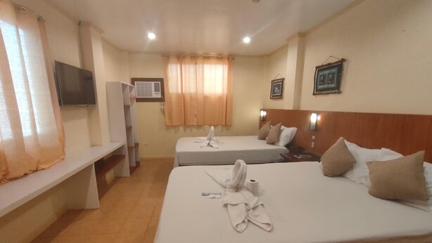A hotel room with two beds, a TV, a desk, and a window with curtains.