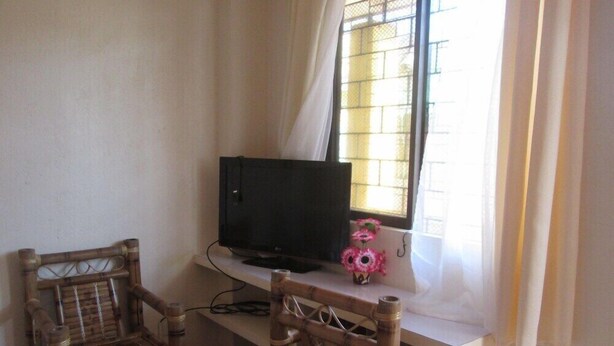 A room with a television on a white stand, two wicker chairs, and a window with a metal grid.