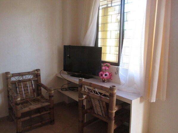 Ein Zimmer mit Fernseher auf einem weißen Schrank, zwei Korbstühle und einem Fenster mit Metallgitter.