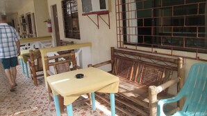 A room with a tiled floor, a wooden bench with a cushion, a table with a tablecloth, and a window with metal bars.