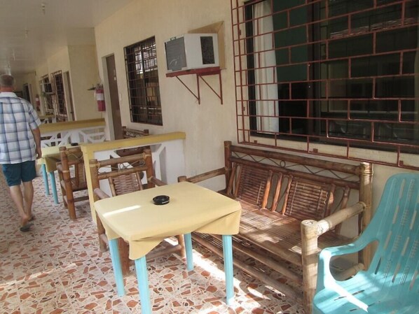 A room with a tiled floor, a wooden bench with a cushion, a table with a tablecloth, and a window with metal bars. - Sulu Plaza Beach Hotel (Boracay Island)