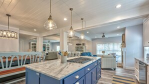 Une cuisine spacieuse dotée d’un îlot central, de meubles de couleur bleue et de luminaires suspendus.