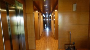 A modern hallway with wooden walls and a polished floor, leading to an elevator and a vent on the right. - Eco Via Lusitana (Madrid)