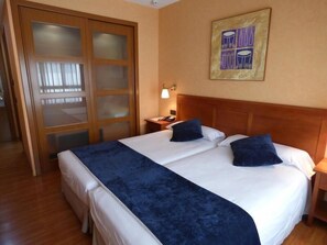 A hotel room with a large bed, a wooden headboard, a nightstand with a lamp, and a door with frosted glass panels. - Eco Via Lusitana (Madrid)