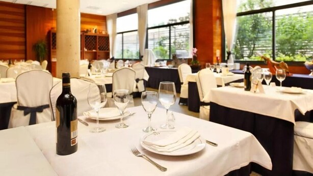 A banquet hall with tables set for dining, large windows, and a view of greenery outside. - Eco Via Lusitana (Madrid)