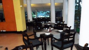 Un restaurant dont les tables et les chaises sont disposées autour d’une colonne centrale, et qui offre une vue sur un paysage tropical grâce à de grandes fenêtres.