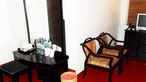 Une pièce comprenant une commode en bois, un miroir, deux chaises, un téléviseur et une moquette rouge.