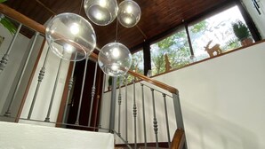 A staircase with wooden railings and a metal handrail, leading to a landing with a view of greenery outside.