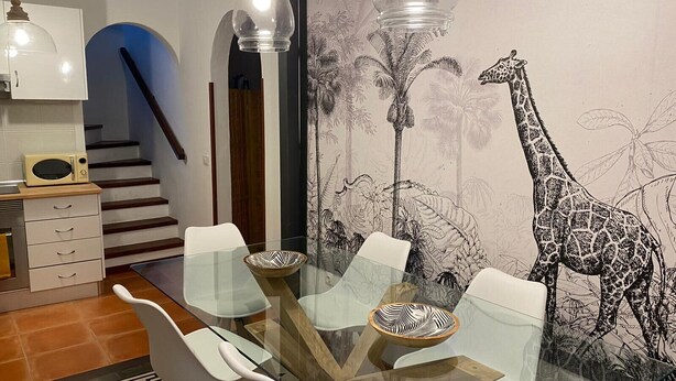 A dining area with a glass table, white chairs, and a giraffe mural on the wall.