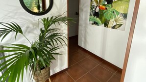 A hallway with a wooden ceiling, a round mirror, a potted plant, and a painting of toucans.