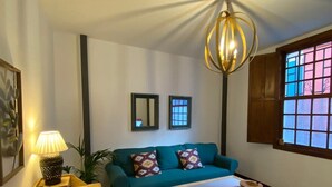 A living room with a teal sofa, patterned rug, wooden coffee table, and a lamp on a wooden side table.