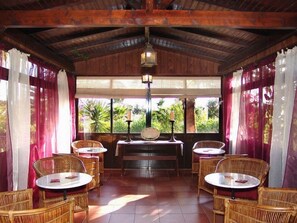 A covered outdoor seating area with wicker furniture and a central table, surrounded by windows with curtains. - Quinta do Mar da Luz Aldeamento (Lagos)