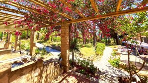 A garden with a pergola covered in pink flowers, a stone pathway, and a pool. - Quinta do Mar da Luz Aldeamento (Lagos)