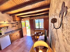 A rustic kitchen with wooden beams, a dining area with a table and chairs, and a view through the window. - Quinta do Mar da Luz Aldeamento (Lagos)