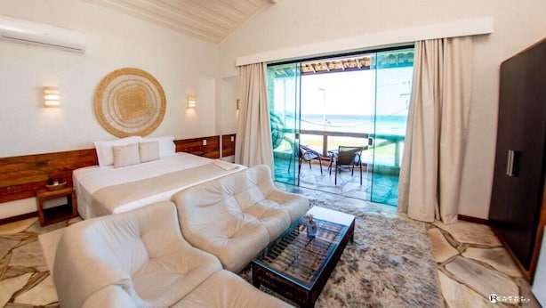 A hotel room with a bed, a sofa, a coffee table, and a view of the ocean through large glass doors. - Pier Beach Hotel (Cabo Frio)