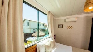 A hotel room with a bed, a window with curtains, a wall-mounted air conditioner, and a small wall decoration. - Pier Beach Hotel (Cabo Frio)