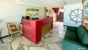 A reception area with a red desk, a wooden chair, a green sofa, and a mural on the wall. - Pier Beach Hotel (Cabo Frio)