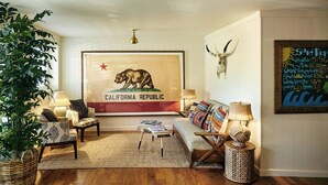A living room with a sofa, two chairs, a coffee table, a large bear poster, a wall-mounted skull, and a surf report. - Laguna Beach House (Laguna Beach)