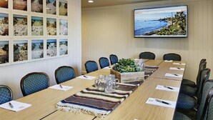 A conference room with a long table, chairs, a projector screen, and a wall with framed pictures. - Laguna Beach House (Laguna Beach)