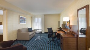 A hotel room with a sofa, a desk with a chair, a small table, and a mirror. - Fairfield Inn Suites By Marriott Paramus (Paramus)