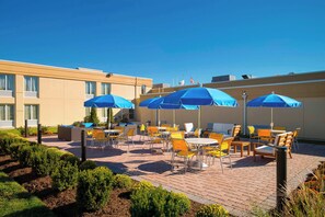 An outdoor patio with tables and chairs, blue umbrellas, and a building in the background. - Fairfield Inn Suites By Marriott Paramus (Paramus)