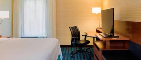 A hotel room with a bed, a desk with a chair, a television, and a window with curtains.