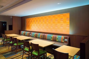 A hotel room with a long bench, multiple tables, and chairs with green cushions.