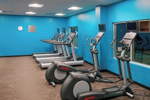 A gym with treadmills and elliptical machines, a clock, and a sign indicating the room's use. - Fairfield Inn Suites By Marriott Paramus (Paramus)