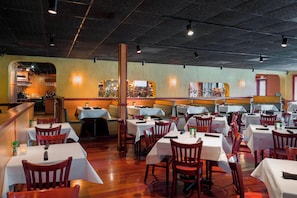 A restaurant with multiple tables and chairs, a bar area, and a view of the kitchen. - Fairfield Inn Suites By Marriott Paramus (Paramus)
