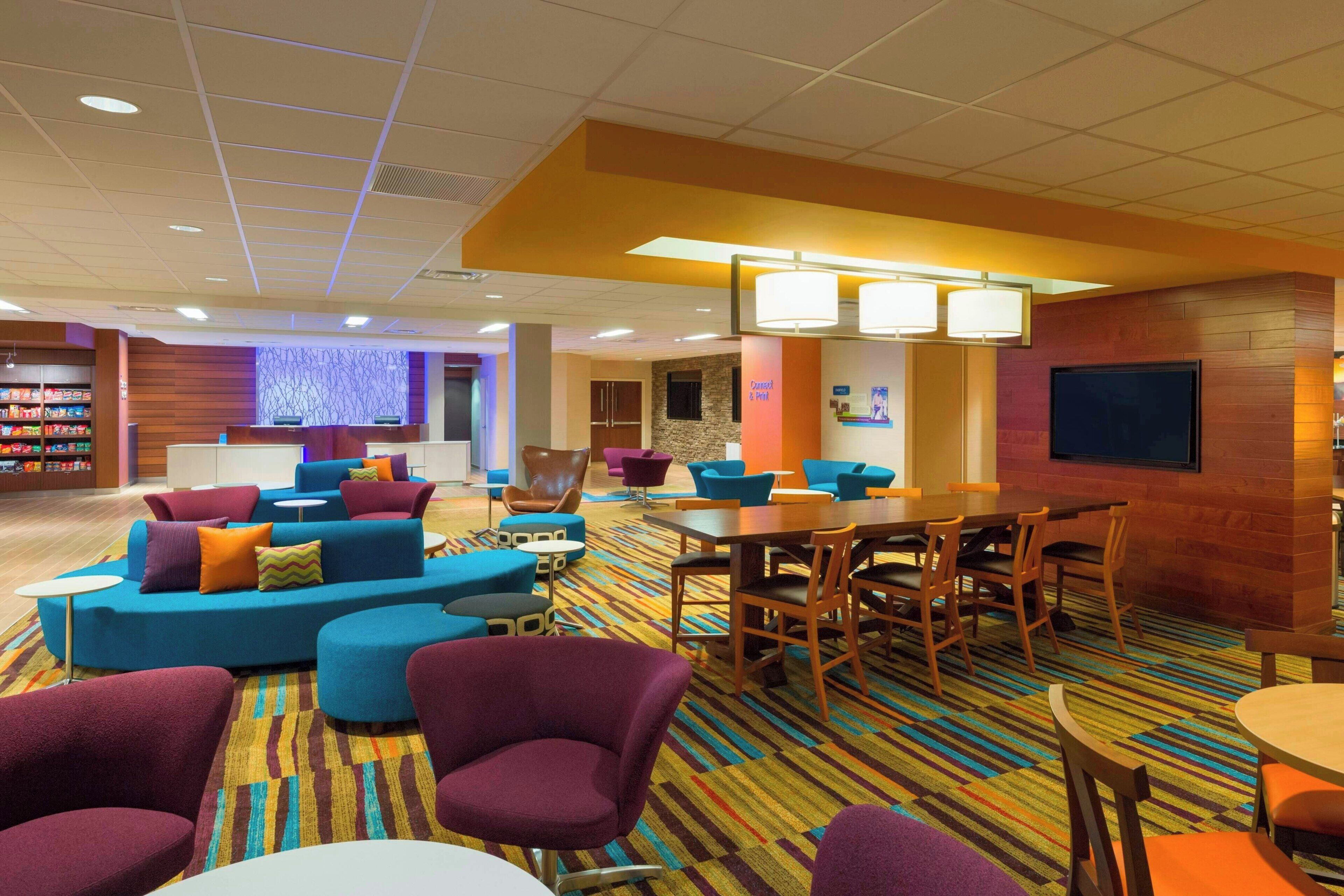 A hotel lobby with seating areas, a reception desk, a TV screen, and a children's play area.