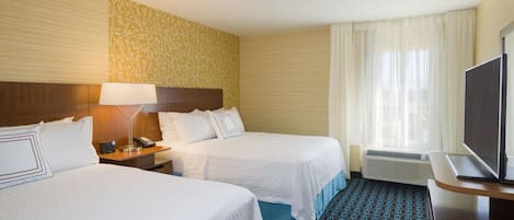 A hotel room with two beds, a bedside table with a lamp, a television, and a window with curtains.