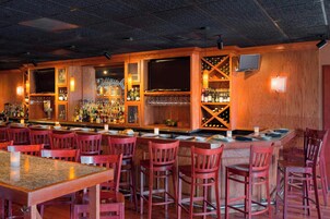Zona de bar con mostradores de madera, sillas rojas y una variedad de botellas y vasos.