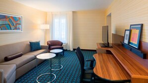 A hotel room with a sofa, two armchairs, a small table, a TV, and a carpeted floor. - Fairfield Inn Suites By Marriott Paramus (Paramus)